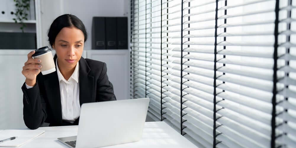 Woman sitting at desk working on computer and holding coffee